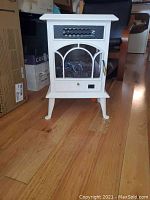 White electric fireplace showing overall front view including legs and glass front with decorative pane design.