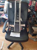 Lasko tower heater on a black chair, showing full unit and control area at base.