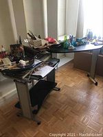 Photo showing desk with cluttered surface including movable side table and keyboard tray, highlighting the desk's metal frame and wheels