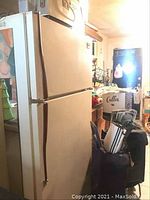 Full side view of the beige Whirlpool refrigerator showing two doors and the surrounding cluttered room.