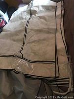 Folded beige fabric wardrobe cover with black piping trim and clear plastic window visible.