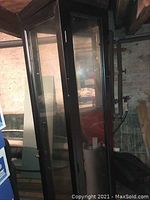 Side and front view of the tall black curio cabinet with glass panels and door, situated in a basement area.