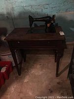 Full view of vintage Singer sewing machine on a wooden treadle table in basement environment