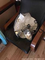 IKEA light fixture and two metal clip-on work lights placed on a black leather office chair. The clip-on lights have silver reflective interior surfaces and attached power cords.