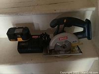 Full view of Ryobi cordless circular saw with battery attached and charger beside it.