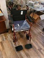 Complete view of the wheelchair showing the metallic orange frame, black cushioned seat and backrest, foldable footrests and wheels