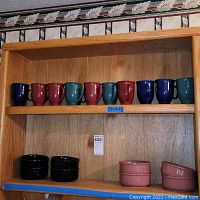 Row of 10 ceramic cups on wooden shelf in a mix of navy, deep red, and dark green colors.