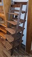 Two brown wooden ladder shelves with slatted shelves in a corner.