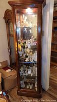 Full view of tall wooden wall cabinet with glass windows displaying decorative items inside.