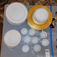 Full view of stacked white porcelain plates and cups with gold trim, and gold chargers from above