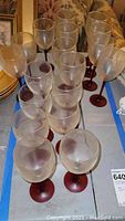 Multiple clear glass wine glasses with red stems and bases arranged on a table.