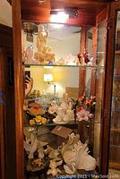 Overview of the wooden cabinet displaying various porcelain figurines such as flowers, animals, and religious figures.