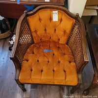 Front view of the wooden armchair showing the burnt orange tufted seat and backrest with cane sides and armrests.