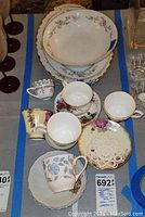 View of 16 china items laid out including multiple tea cups, saucers, bowls, and platters with various floral patterns and gold trim details.