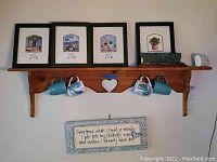 Photo of a wooden wall shelf mounted on the wall with heart cut-out feature holding four ceramic coffee mugs, four framed pictures, a marble plaque, and a carbon monoxide alarm (excluded).