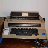 Front view of beige IBM electric typewriter with keyboard and paper holder.
