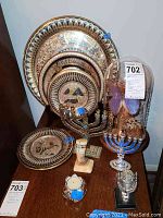 Full view of ten metalware items including plates, menorah, butterfly case, and various decorative statues on a shelf.