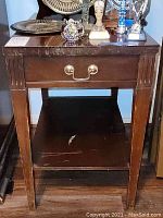 Front view of the solid wood end table showing drawer with metal handles, smooth top surface, lower shelf with scratches.