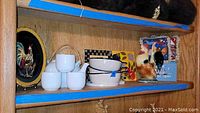 Shelf with mixed ceramics including white tea cups, ceramic bowls, a rooster figurine, and other ceramic items