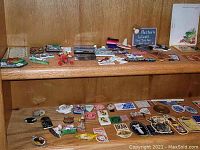 Shelf showing a collection of over 30 assorted magnets placed in rows featuring various designs including animals, states, and humorous sayings.