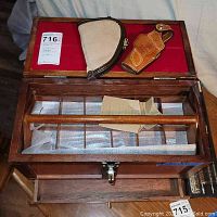 Top view of the wooden box opened showing the red-lined top compartment holding two leather gun holsters and visible bottom drawer