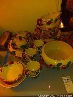 Full set of Franciscan earthenware dishes showing cups, bowls, and plates stacked, highlighting the vine and leaf handles with red fruit decoration.