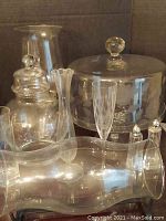 Photo showing glass vases, jar with knob lid, flute glass, and salt shakers against a cardboard background.