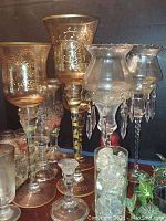 Wide view showing various sizes and styles of glass candle holders including amber goblet style and tall clear holders with hanging crystals along with a tray holding smaller votive holders and tea lights.