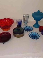 Photo showing assorted vintage glassware including ruby red carnival glass bowl, blue daisy candle holders, various small glass vessels and dishes.