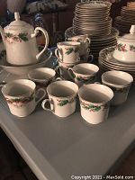 Close-up photo of Christmas dinnerware featuring cups, teapot, and plates decorated with holly and ribbons.