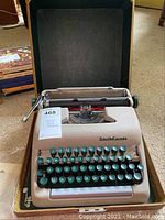 Photo of the vintage Smith Corona Clipper portable typewriter positioned inside its open beige hard case, showing the full typewriter with keys and carriage return lever visible.
