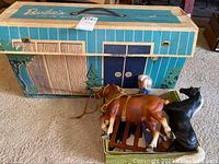 Original cardboard box for vintage Barbie Dream House with carry handle and visible wear on carpeted floor with two toy horses beside it.