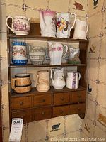 Full view of wooden wall-mounted shelf holding 13 ceramic creamers and pitchers of various colors and designs