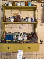 Full view of yellow wall shelf mounted on wall displaying a large varied collection of vintage salt and pepper shakers and small containers.