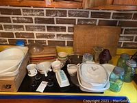 Countertop with multiple vintage kitchen items including Pyrex dishes, butter dish, Mason jars, cups, and wooden boards.