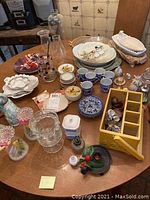Overview of assorted glassware, plates, cups, saucers, miniatures, and figurines on a wooden table