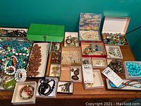 Wide view showing numerous boxed and loose beaded necklaces in turquoise, white, green, and black hues alongside boxes containing bracelets and pins.