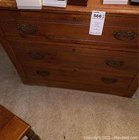 Front view of antique wooden chest of drawers showing three drawers with bronze-tone metal handles and signs of use, including scratches.