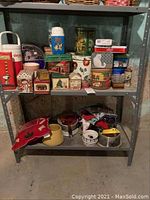 Wide view of metal shelving with assorted novelty and themed tins, dog bowls, and pillow underneath