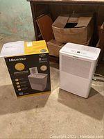 Hisense Dehumidifier and original box placed on basement floor with some cardboard boxes behind.