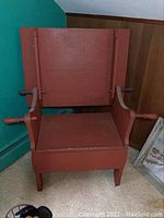 Front view of the wooden red convertible chair with armrests, showing the chair form with the backrest upright.