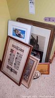 Photo showing multiple framed artworks, prints, and pet photographs leaning against a wall including a large rabbit sketch and a cat photo.