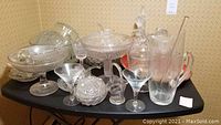 Wide view of crystal and cut glass barware and stemware including a pedestal bowl, glasses, decanters, and souvenir tray.