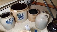 Four vintage stoneware crocks and jug shown together on floor near wall, PVC pipe and tripod stand in corner.