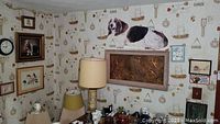 View of wall with framed dog art, cat embroidery and other wall decorations, lamp and shelves with glassware.