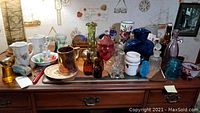 Collection of various glass, ceramic, and collectible items on a wooden dresser, showing the range and styles of bottles, vases, insulators, plates and figurines.