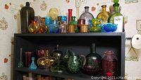Front view of entire collection of vintage apothecary bottles and glassware on two shelves showing a wide range of colored glass pieces.