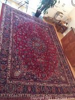 Overhead full view of red Persian Mashad rug with central floral medallion, navy and beige borders, placed on hardwood floor