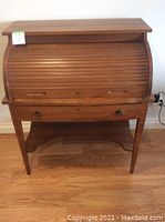 Front view of antique rolltop desk closed, showing slatted rolltop and lower drawer with handles, resting on tapered legs.