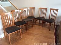 Front angled view of six wooden dining chairs arranged in a curve on hardwood floor, showing the cushioned seats and cherry wood vertical slat backs.